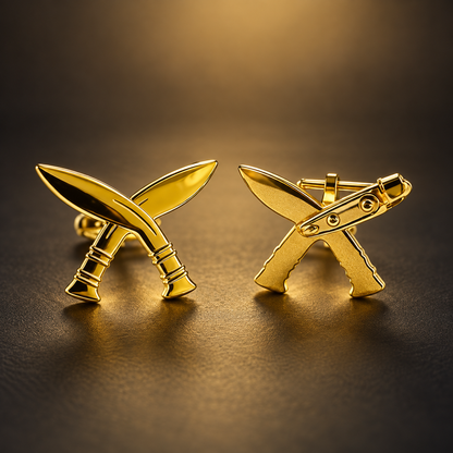 A pair of gold-tone cufflinks shaped like crossed curved blades, photographed on a dark textured surface with a warm spotlight background.