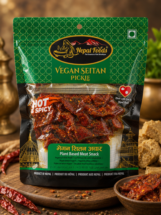 A stand-up pouch of Nepal Foods Vegan Seitan Pickle, featuring a green and black design with a clear window showing the spicy red-brown seitan slices inside. The package is displayed on a wooden board with dried red chilies and a small bowl of the pickle in a rustic, warm-toned setting.